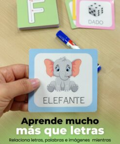 Mano sosteniendo una tarjeta ilustrada con un elefante y la palabra en punteada para repasar, con tarjetas de letras y un marcador borrable, de fondo una mesa de madera.
