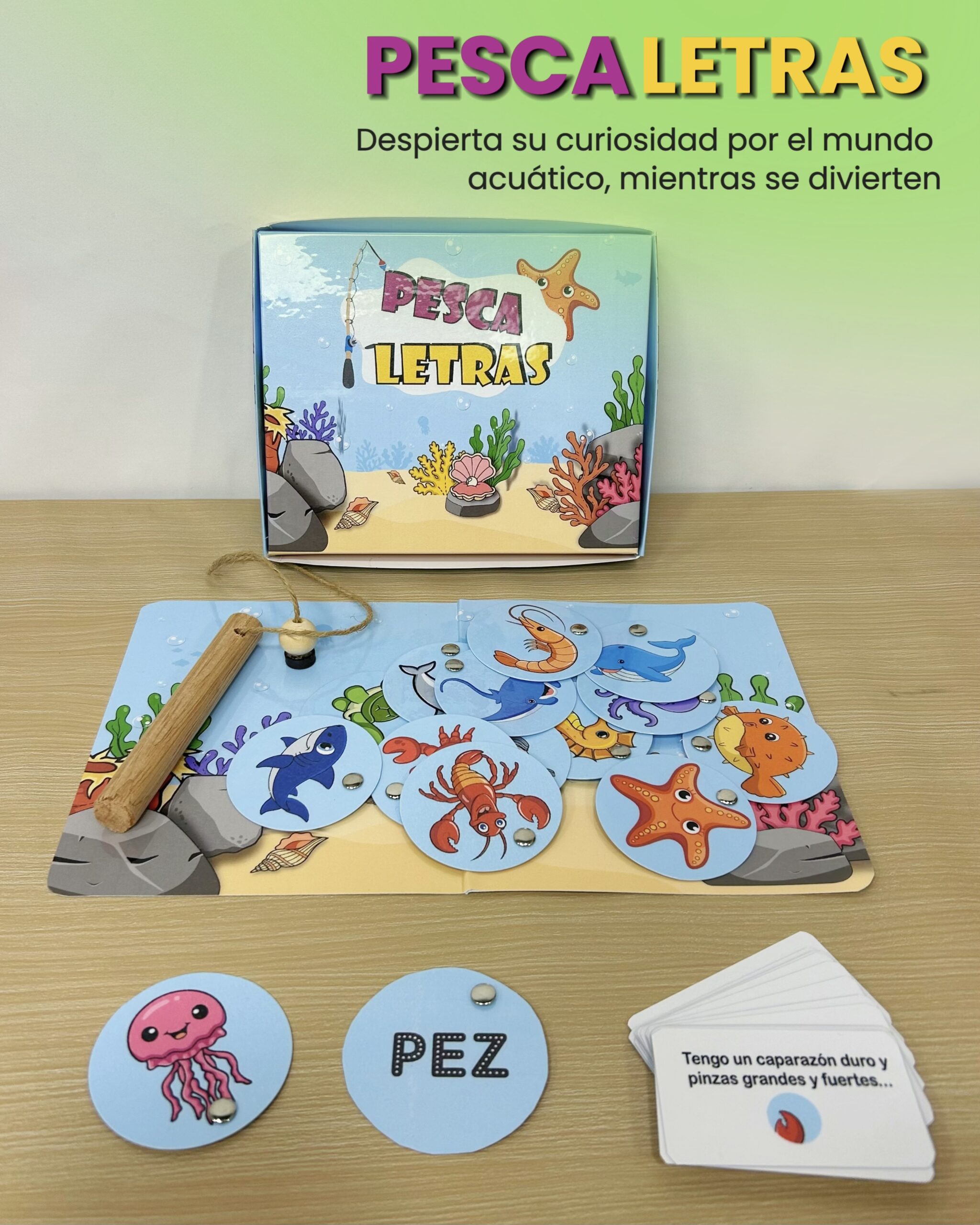 Juego de mesa didáctico Pescaletras en su caja decorada con el tema marino, acompañado del tablero, caña de pescar, tarjetas de adivinanzas