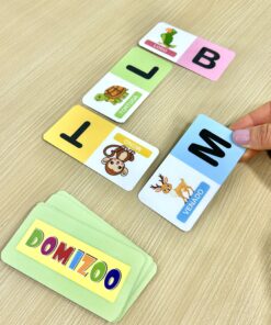 Mano colocando una tarjeta del juego Domizoo para asociar la letra M con la inicial del venado sobre mesa de madera.