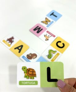 Mano mostrando la ficha de la tortuga y la letra L sobre una secuencia de juego de dominó Domizoo armado.