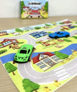 Vista de cerca de un autito de juguete verde sobre la pista de un tapiz infantil de tela impreso con ilustración de escuela y comisaría.