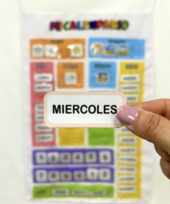Primer plano de una mano mostrando la tarjeta con la palabra Miercoles frente al calendario didáctico de tela.