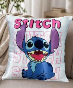 Almohadón blanco satinado con el personaje de stitch sonriendo bajo su nombre en letras rosadas, apoyado en un sillón moderno con una manta tejida de fondo.