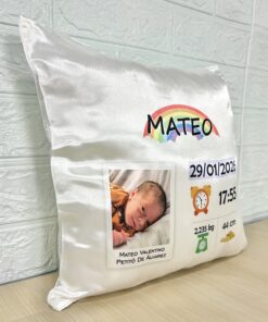 Vista en perspectiva de tres cuartos de un almohadón satinado personalizado de nacimiento, sobre una mesa de madera. Mostrando el volumen de relleno y textura brillante.