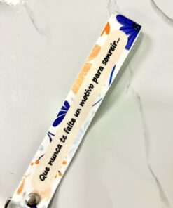 Llavero de cinta textil sublimado con estampado floral y la frase Que nunca te falte un motivo para sonreir.
