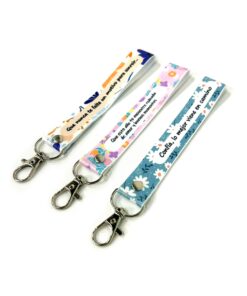 Tres llaveros de cinta personalizados con mosquetón metálico y diferentes frases e ilustraciones florales.