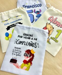 Cuatro modelos de bolsitas golosineras de tela con diferentes diseños personalizados de cumpleaños sobre mesa de madera.
